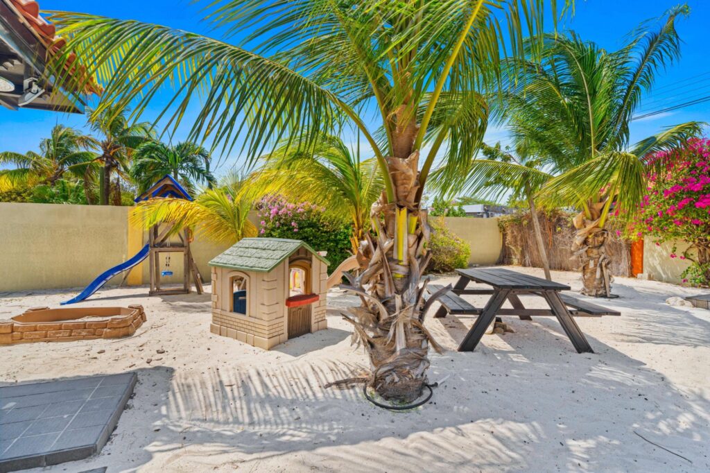 Sandy garden play area with palm trees and picnic table
